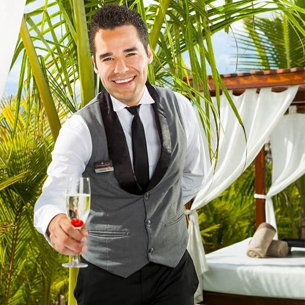 A waiter at Karisma Resorts holding a glass of champagne in front of a palm tree. A waiter at Karisma Resorts holding a glass of champagne in front of a palm tree.
