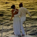 A couple enjoying a destination wedding on the bow of a boat at sunset.