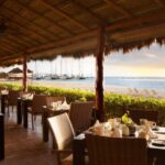 A Secrets Maroma Beach restaurant with tables and chairs overlooking the ocean.