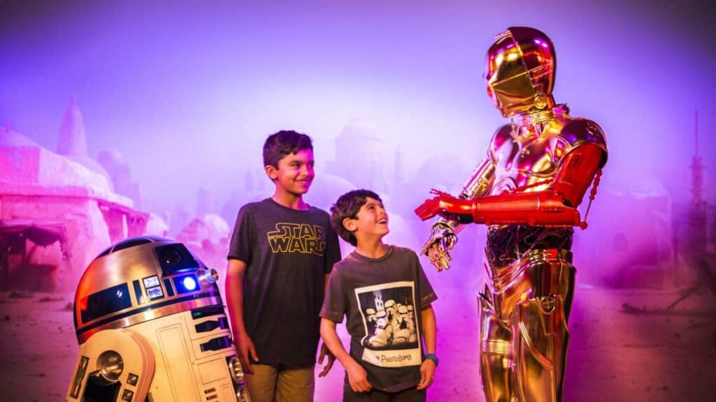 A group of kids excitedly posing next to a Star Wars Cruise-inspired R2-D2.