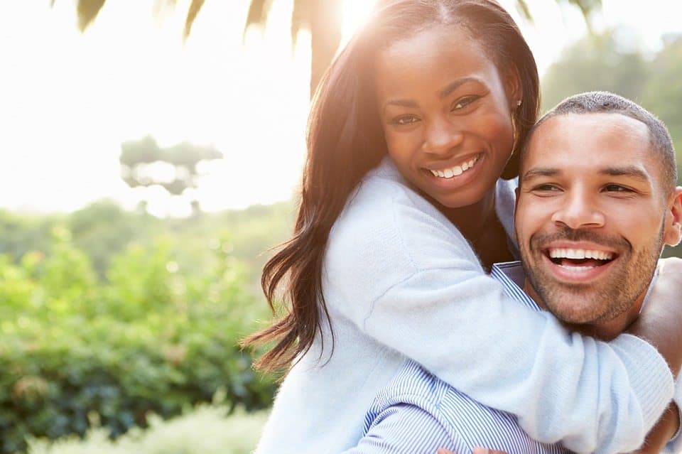 A man and woman embrace in front of a palm tree.
