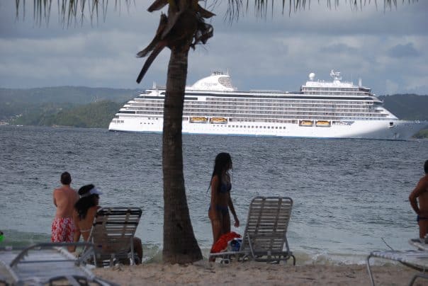 People are sitting on the beach near a Regent Seven Seas cruise ship.