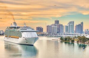 A cruise ship sails past a city skyline with skyscrapers in the background during a dreamy vacation.