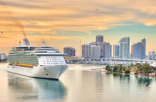 A cruise ship sails past a city skyline with skyscrapers in the background during a dreamy vacation.