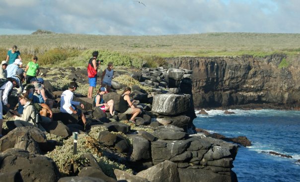 A group of people standing on a Galapagos Islands cliff overlooking the ocean.