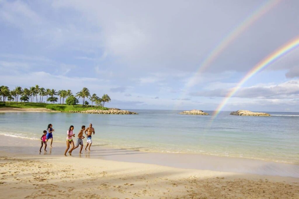Three people standing on a beach at Aulani Disney Resort with a rainbow in the sky.