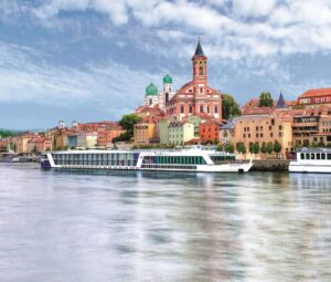 A Disney cruise ship navigates a river with a scenic cityscape in the background.