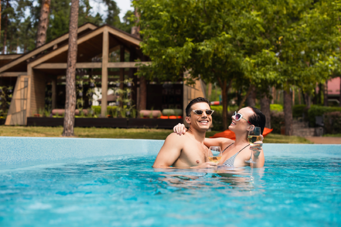 Brunette woman with wine hugging boyfriend in swimming pool on resort
